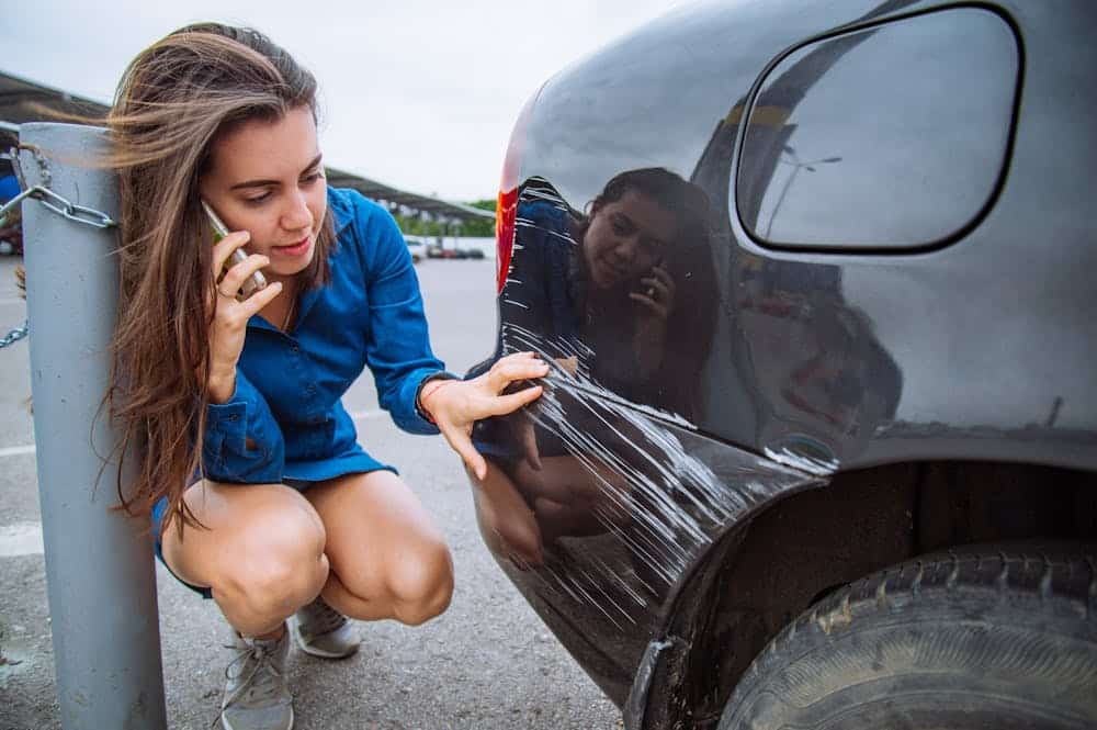 File a Police Report – Personal Injury Lawyer in Fort Lauderdale Woman examining car scratch while on phone, wearing a blue shirt.